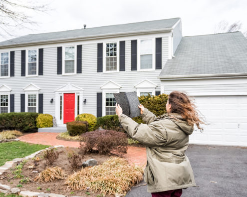 Woman holding roofing shingles outside a home on a windy day