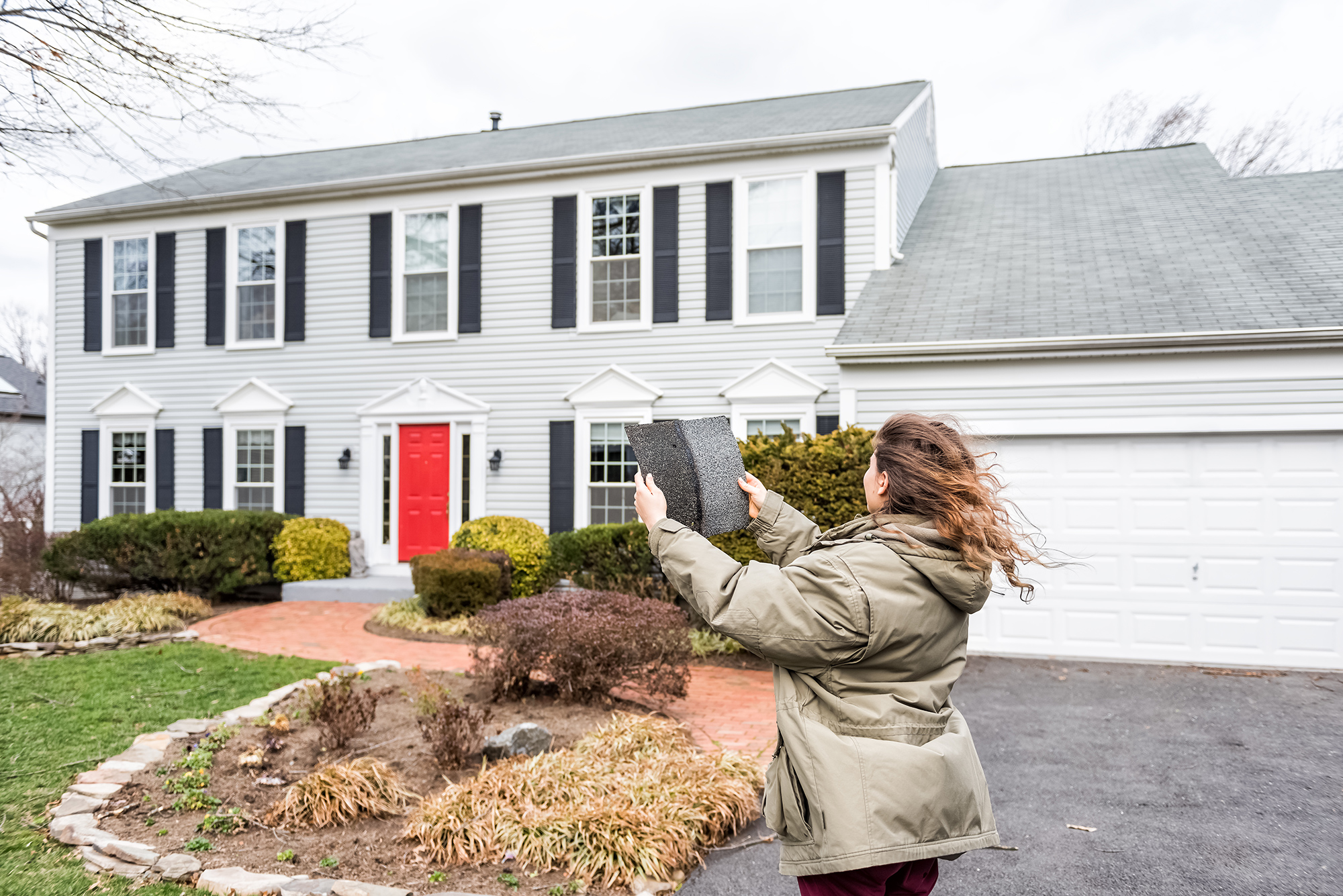 Woman holding roofing shingles outside a home on a windy day